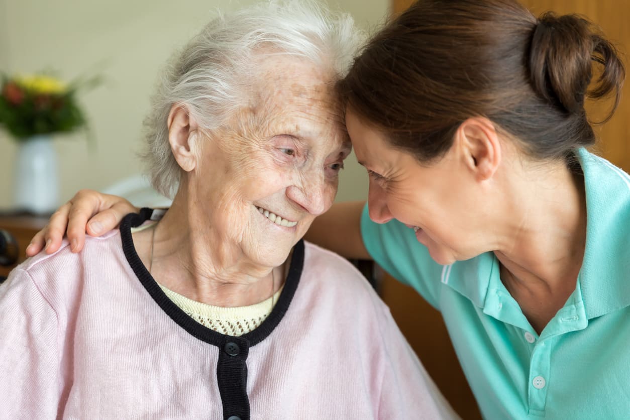 Demenzpatientin und Pflegerin lehnen ihre Köpfe aneinander