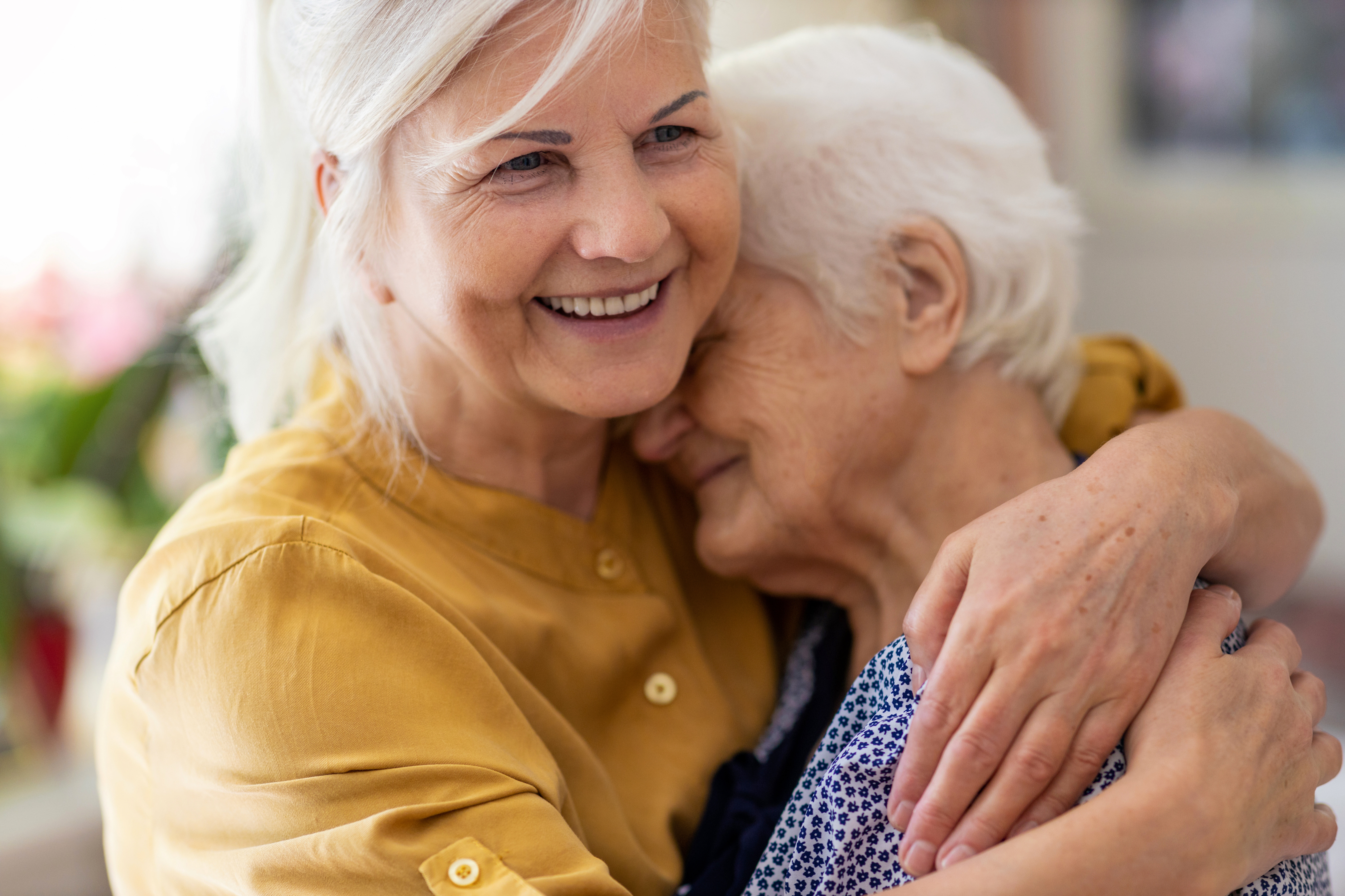 Ältere Frau nimmt eine andere ältere Frau in den Arm. Das Bild steht symbolisch für eine Frau, die eine Betroffene von Alzheimer oder Demenz tröstet