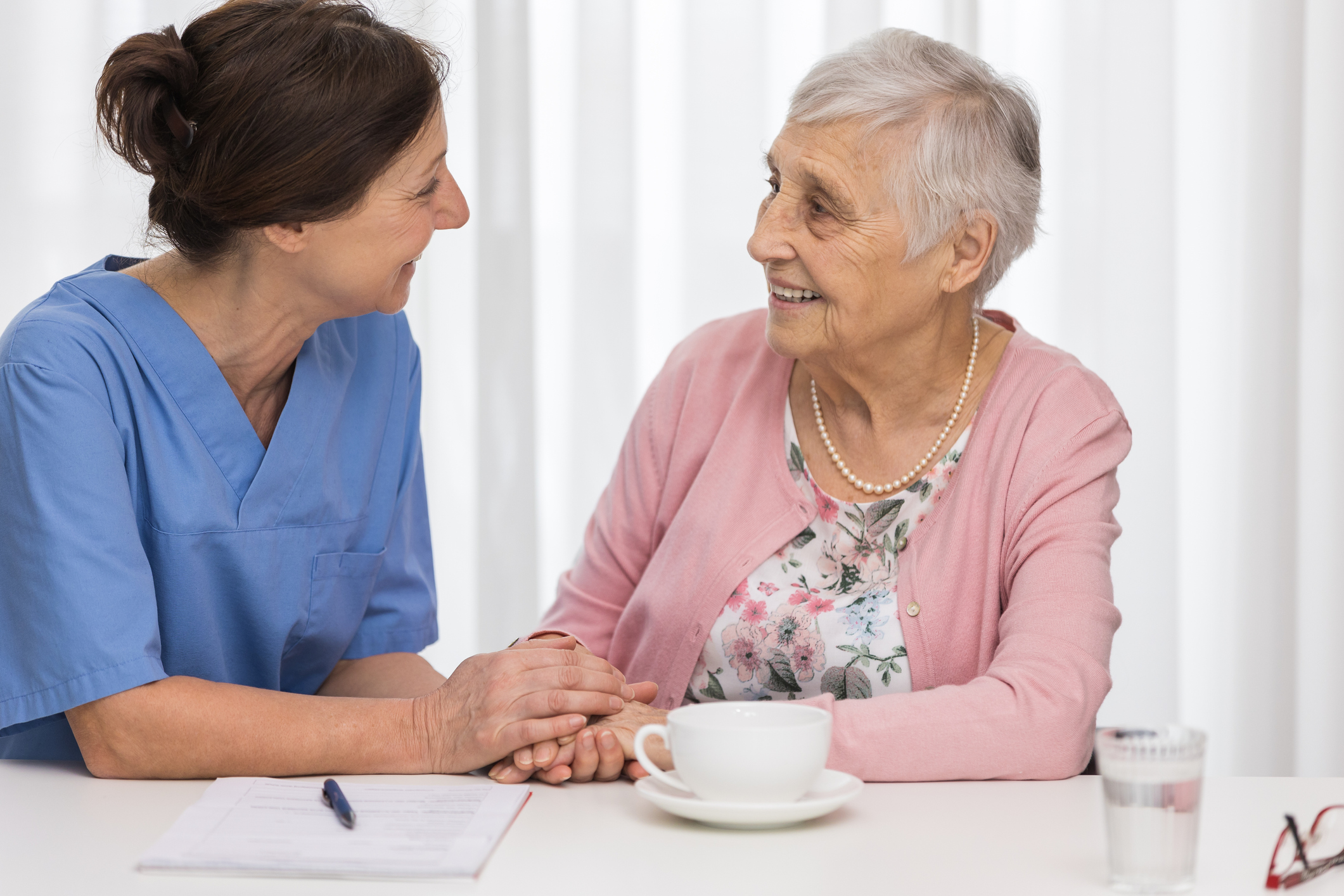 Eine Pflegekraft hält die Hand einer Seniorin und sie scheinen sich freundlich zu unterhalten. Das Bild steht sinnbildlich für den Zeitgewinn, den Pflegedienste durch die Zusammenarbeit mit hellomed erwarten können.